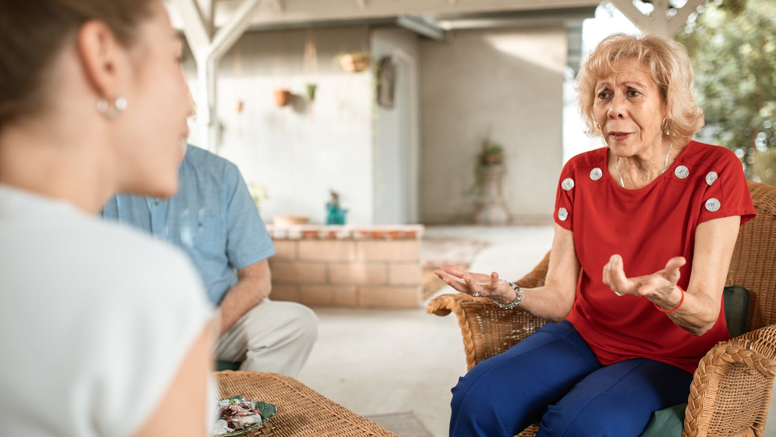 An older woman in mid-conversation with her adult daughter on a sunlit patio
