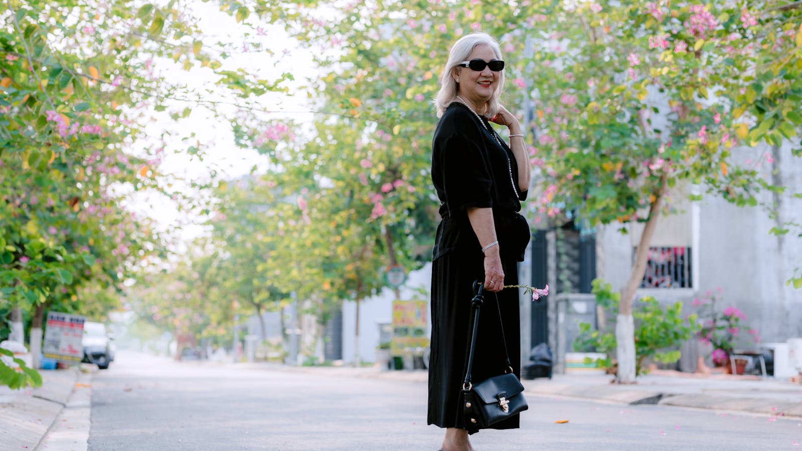 An older woman walking on a sunlit, tree-lined street in her neighbourhood